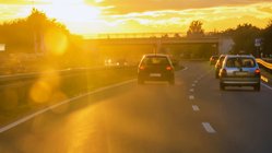 Fahrzeuge auf Autobahn, im Hintergrund blendet tief stehende Sonne.