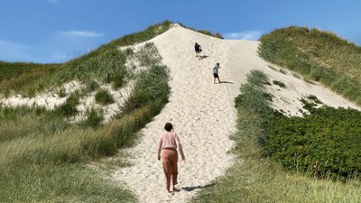 Drei Personen beim Aufgang zu einer Düne am Sandstrand.